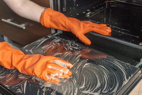 Kitchen cleaning. Girl's hands in gloves wash clean the stove, kitchen oven in the kitchen.